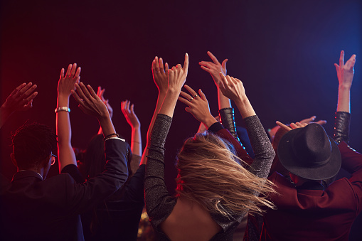 Back view of young people jumping and raising hands while enjoying party in smoky nightclub, copy space