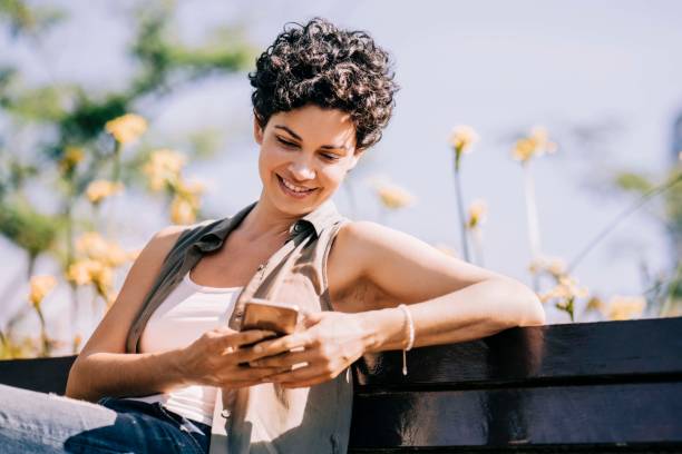 istock Happy female text messaging while sitting in park 1192895722