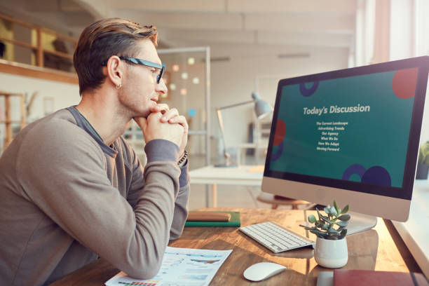 Businessman Working on Presentation Side view portrait of adult businessman looking at computer screen while preparing for presentation or online conference at desk in office, copy space presentation on computer stock pictures, royalty-free photos & images