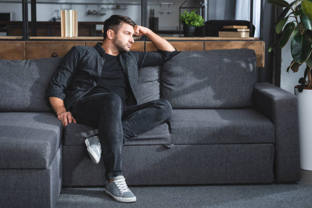 istock handsome and pensive man sitting on sofa in apartment 1192896191