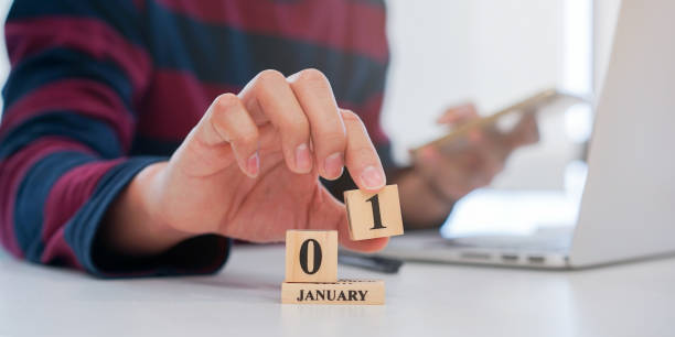 nahaufnahme mitarbeiter mann hand setzen nummer 1 von würfel form holz, um einen neuen make-kalender-datum im januar am büro schreibtisch für den ersten tag des neuen jahres countdown-konzept zu starten - year block cube new years eve stock-fotos und bilder