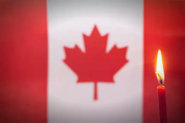 Burning candle on the background of the flag of Canada. The concept of mourning and sorrow in the country