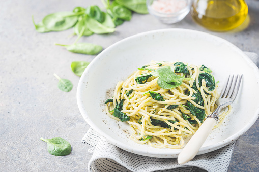 Spaghetti pasta with spinach and green pesto, in a white plate on gray stone background