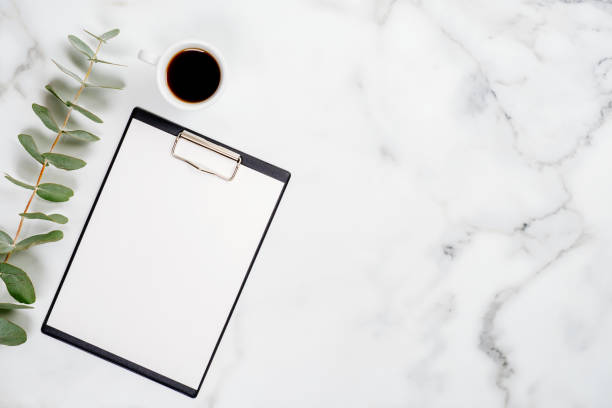 istock Clipboard with blank paper note, cup of coffee and eucalyptus on marble background. Flat lay, top view. Home office desk table concept. 1192899898