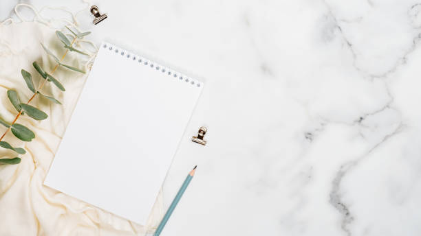 istock White marble background with blank paper notepad, eucalyptus, scarf and office supplies. Flat lay, top view, copy space. Home office desk table concept. 1192899903