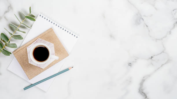 istock Home office desk with paper notepad, cup of coffee and eucalyptus leaf on marble background. Feminine workspace concept. Flat lay, top view, copy space. 1192900007