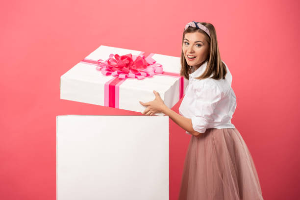 istock attractive and smiling woman opening gift box isolated on pink 1192901113