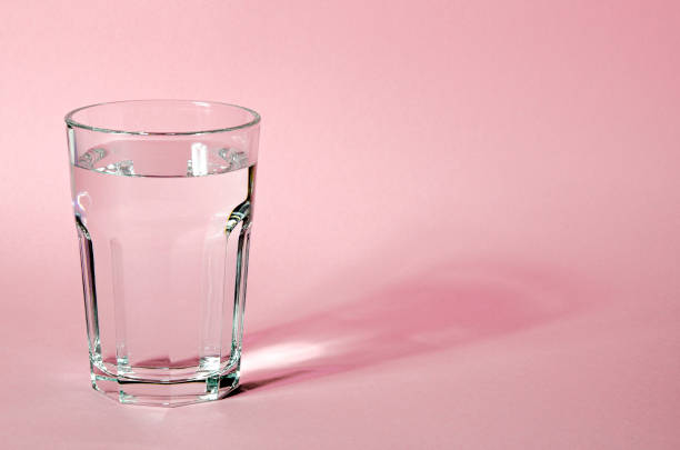 Water glass with strong shadows on pink background Glass beaker from which padajet sharp shadow, stands on a pink background. Empty space for text glass of water stock pictures, royalty-free photos & images