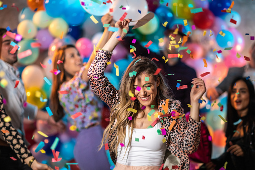 Young woman dancing and having good time with friends while confetti falling down at house party