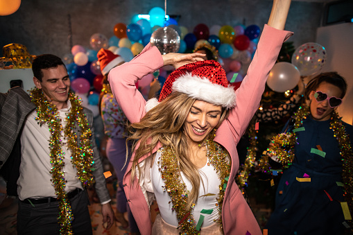 Beautiful young woman wearing santa hat, dancing and having fun with her friends during new year's eve party