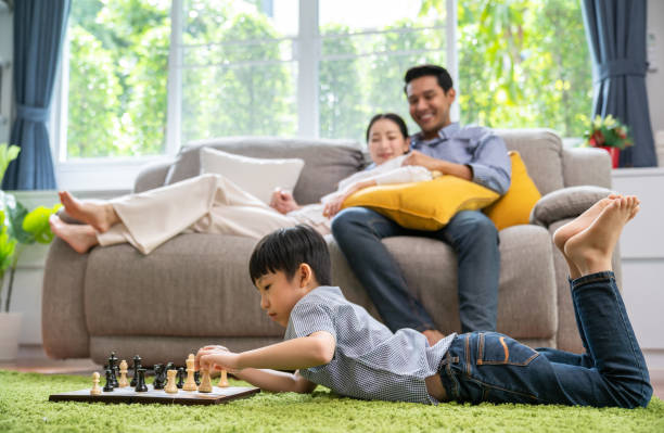 Parents looking at their children happiness playing chess in the living room stock photo