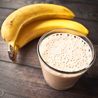 Glass of banana smoothie and fresh bananas on brown wooden background