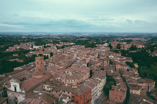 Panoramic view of Siena city with historic buildings and far away green fields from Torre del Mangia is a tower in city. Summer sunny day and dramatic blue sky