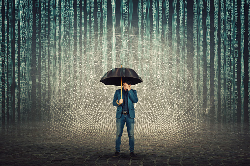 Businessman hiding face standing under umbrella shield to protect of internet viruses as matrix code numbers falling above like a rain. Anonymous personal data thief. Antivirus and firewall concept.