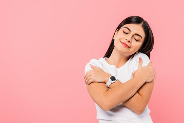 smiling pretty brunette girl hugging herself with closed eyes isolated on pink smiling pretty brunette girl hugging herself with closed eyes isolated on pink hugging self stock pictures, royalty-free photos & images