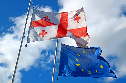 Georgian flag and EU Flag Waving on Sunny Blue Sky