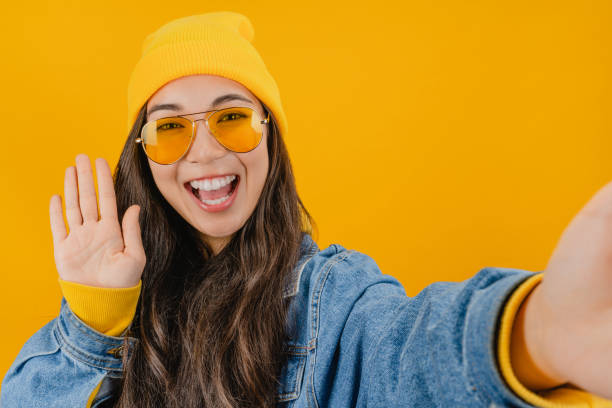 istock Close up of woman using cellphone showing Hi gesture while making video call over yellow background 1192933149