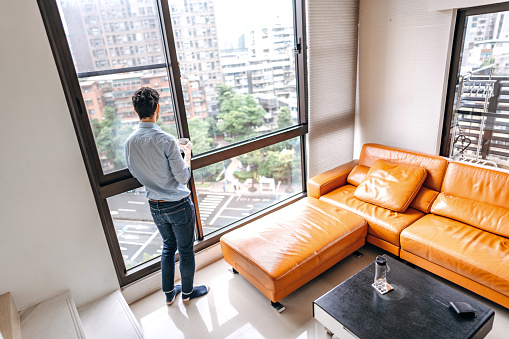 Mid adult man drinking coffee and looking out through window of his modern apartment