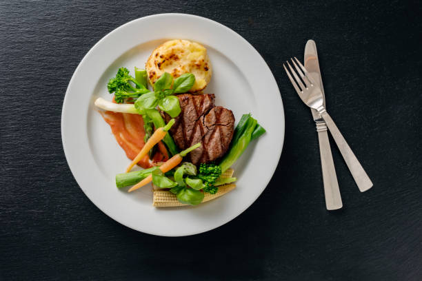 Overhead view of a main course dish of veal tenderloin with seasonal vegetables which include carrots and leeks with a potato gratin and a tomato sauce. Colour, horizontal with some copy space. Shot on location in a restaurant on the island of Moen in Denmark.