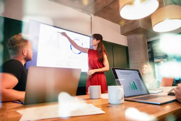 Photo of Confident business woman presents quarterly progress in meeting using a large display screen