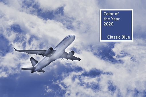Flying high airplane in beautiful scenery blue sky among the white clouds lit with sun beams with copy space. Travel and vacation concept. Main color trend of the year 2020.
