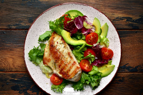 istock Grilled chicken breast with vegetable salad on a white plate over dark rustic wooden background. 1192946277