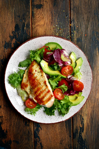 istock Grilled chicken breast with vegetable salad on a white plate over dark rustic wooden background. 1192946324