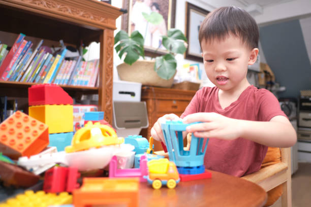 おもちゃで遊ぶ幼児、かわいいアジアの幼児の男の子は、自宅で屋内でカラフルなプラスチックブロックで遊んで楽しいです - fine motor skills ストックフォトと画像