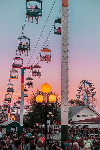 Des Moines, Iowa / United States - August 10, 2018: Sunset scene of crowds of people, a ferris wheel, Ye Old Mill and the Sky Glider at the Iowa State Fair, Des Moines, Iowa, USA.