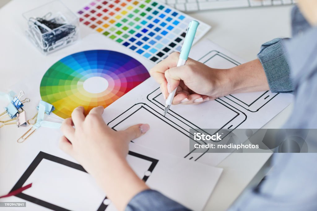 Close-up of unrecognizable designer sitting at desk with papers and drawing interface design for digital devices Making interface design for digital devices Design Stock Photo