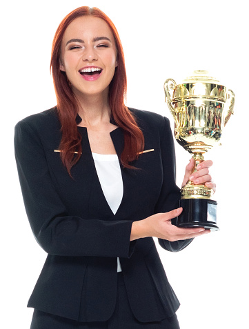 Front view / one person / waist up / portrait of 20-29 years old adult beautiful redhead / long hair caucasian female / young women businesswoman / business person standing wearing businesswear / a suit who is smiling / happy / cheerful / laughing / successful and winning / showing award who is in first place and holding trophy - award