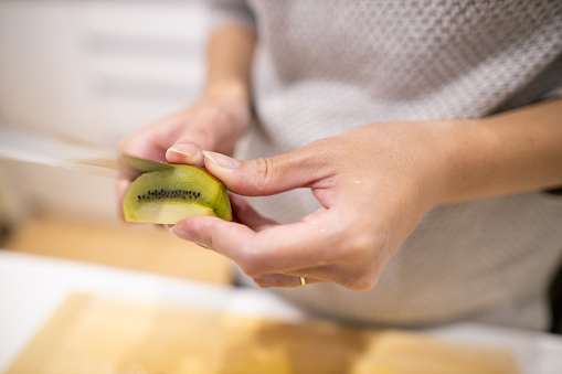 Young woman peeling kiwi in kitchen