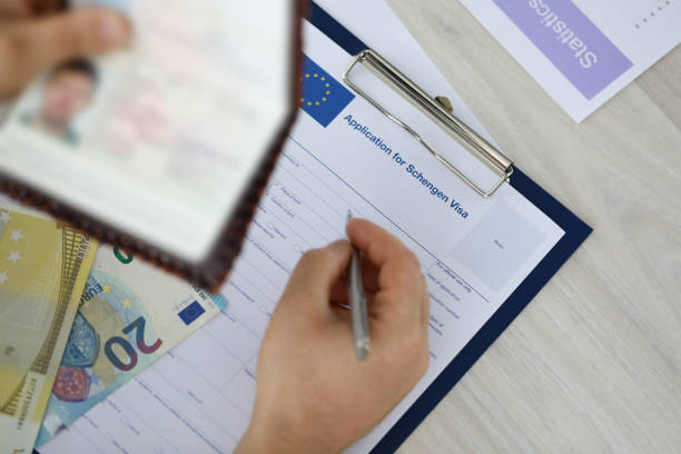 Man drawing up forms Focus on male holding identity documents and filling application for schengen visa Businessman sitting at wooden table. Travelling abroad or immigration concept. Blurred background schengen agreement stock pictures, royalty-free photos & images
