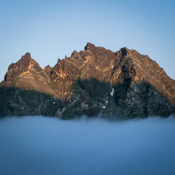 Mountain peaks emerge from the sea of clouds, catching first rays of light at sunrise. stock photo