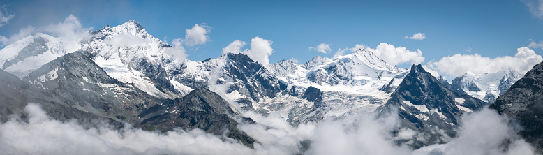 Dramatic scenery full of sharp 4000m peaks covered in snow and glacial ice, emerging from jagged clouds.