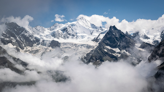 Dramatic scenery. Sharp 4000m peaks covered with glaciers and blinding white snow, emerge from jagged clouds.