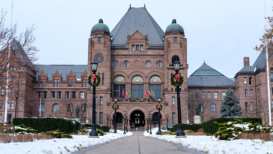 Toronto, Ontario, Canada 12/08/2019: Front facing scene of winter holiday season at Queen's Park Legislative Assembly of Ontario in Toronto, ON. Flags and holiday decor on the brownstone legislative building.