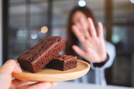 A woman making hand sign to refuse a brownie cake in wooden plate from someone