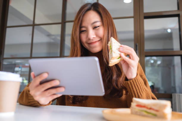 istock woman holding and eating whole wheat sandwich while using tablet pc 1192991150