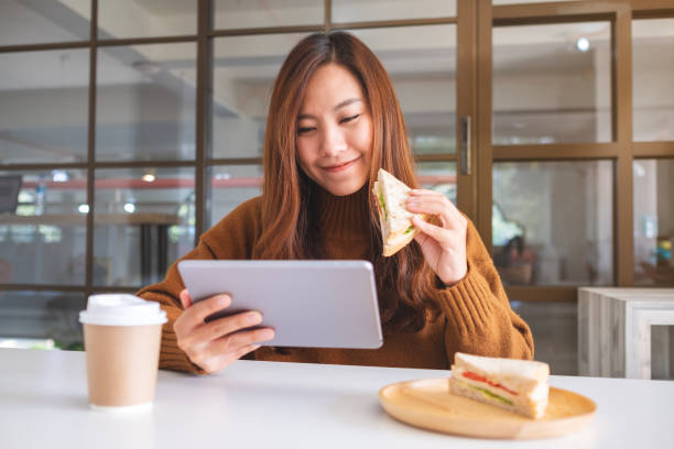 istock woman holding and eating whole wheat sandwich while using tablet pc 1192991784