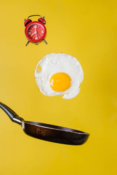 istock Breakfast time. A fried egg and a frying pan with a watch levitate in the air on a yellow background 1192995403