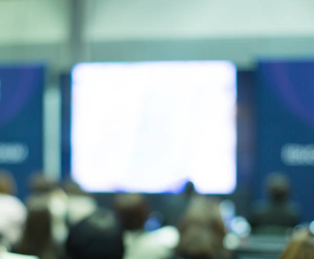 istock Blurred De-focused Audience in Conference Lecture Presentation Room. Corporate Presentations in Conference Hall. Seminar Speaker Giving Training to New Employees. Blank copy space presentation screen 1192998077
