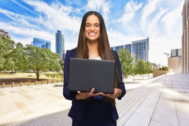 waist up / portrait / front view / looking at camera / one person of beautiful african ethnicity / african-american ethnicity female / young women business person / businesswoman standing who is outdoors wearing a suit / cool attitude who is working - looking up young women outdoors laptop imagens e fotografias de stock