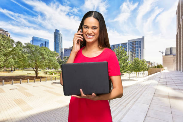 waist up / portrait / front view / looking at camera / one person of beautiful african ethnicity / african-american ethnicity female / young women standing who is outdoors who is smiling / happy / cheerful / laughing / talking / cool attitude - looking up young women outdoors laptop imagens e fotografias de stock