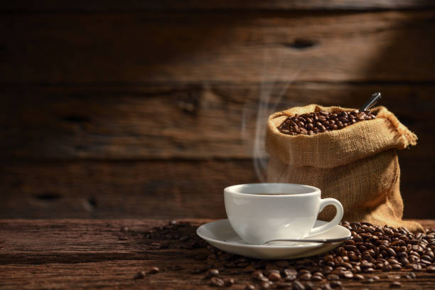 Cup of coffee with smoke and coffee beans on old wooden background Cup of coffee with smoke and coffee beans on old wooden background sack photos stock pictures, royalty-free photos & images