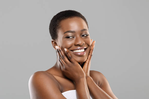 Attractive black girl touching her smooth skin on cheeks Face massage. Attractive african american woman touching her smooth flawless skin on cheeks, posing over gray background with copy space black skin stock pictures, royalty-free photos & images