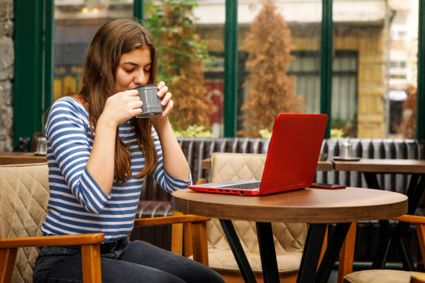 istock Young Woman Drinking Coffee and Using Laptop in a Cafe 1193035324