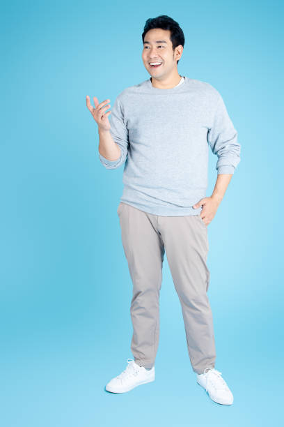 Happy Asian man wearing gray sweater standing on blue background.