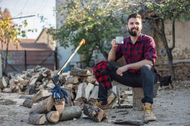 Young attractive man having a cup of hot coffee after cutting firewood in the backyard