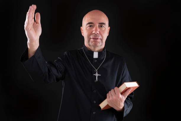 istock Priest holding bible hairless in low key black 1193047394